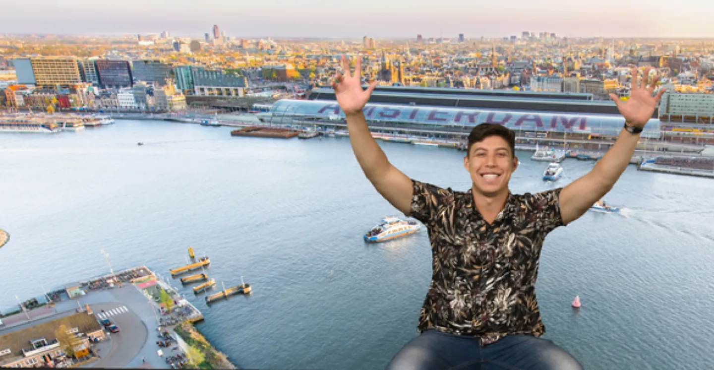 Lucas em uma viagem, em um mirante com uma cidade e a água ao fundo